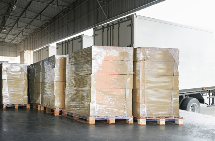 Packaged shipments wrapped in plastic stacked on pallets waiting to be loaded onto a semi truck.