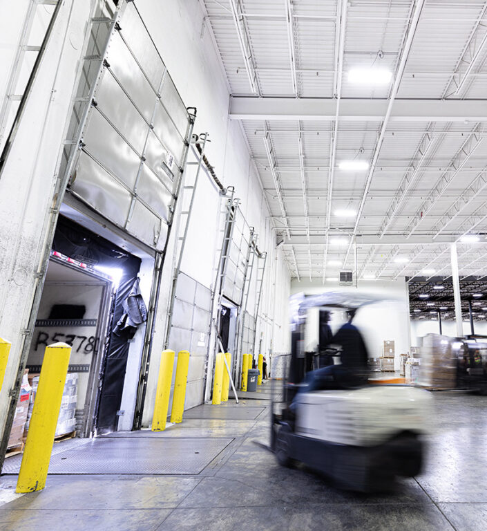 Two forklifts loading a semi truck parked at a loading dock full of freight. 