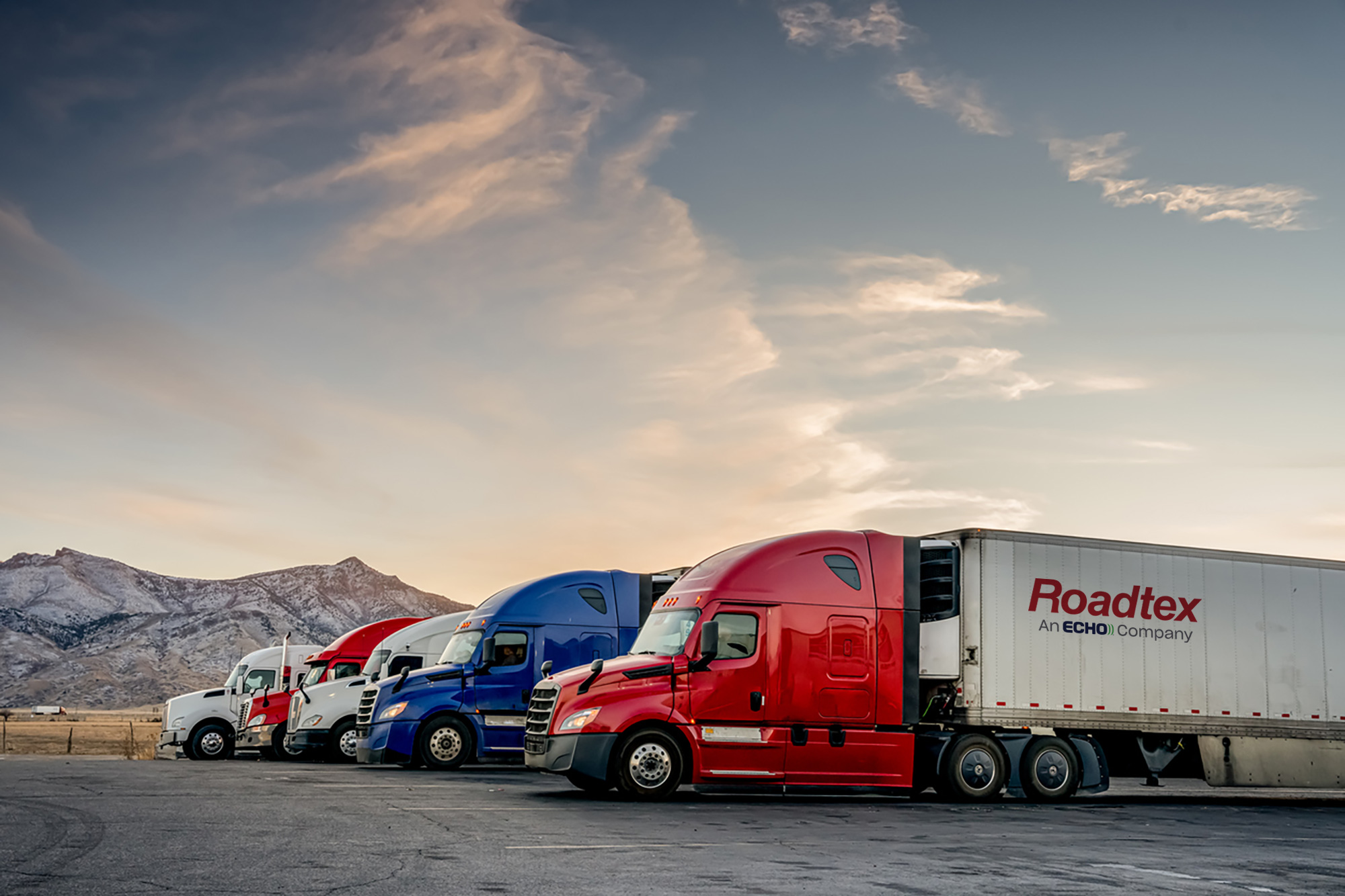 Red, blue, and white semi trucks parked in a row in a parking lot.