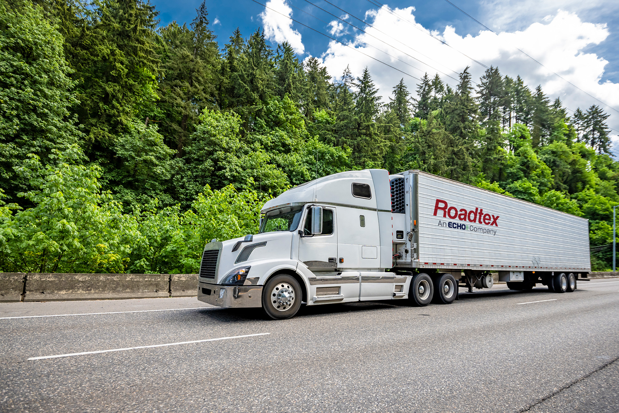 A white semi truck driving down a tree lined highway.