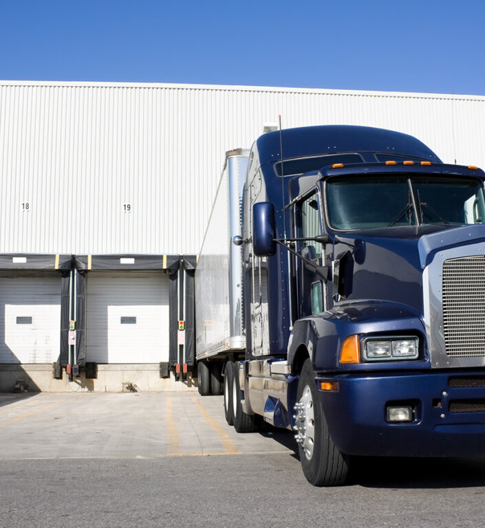 A blue semi truck parked in a loading dock.