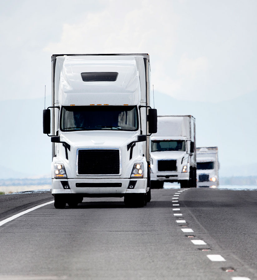 Three white freight trucks on a highway