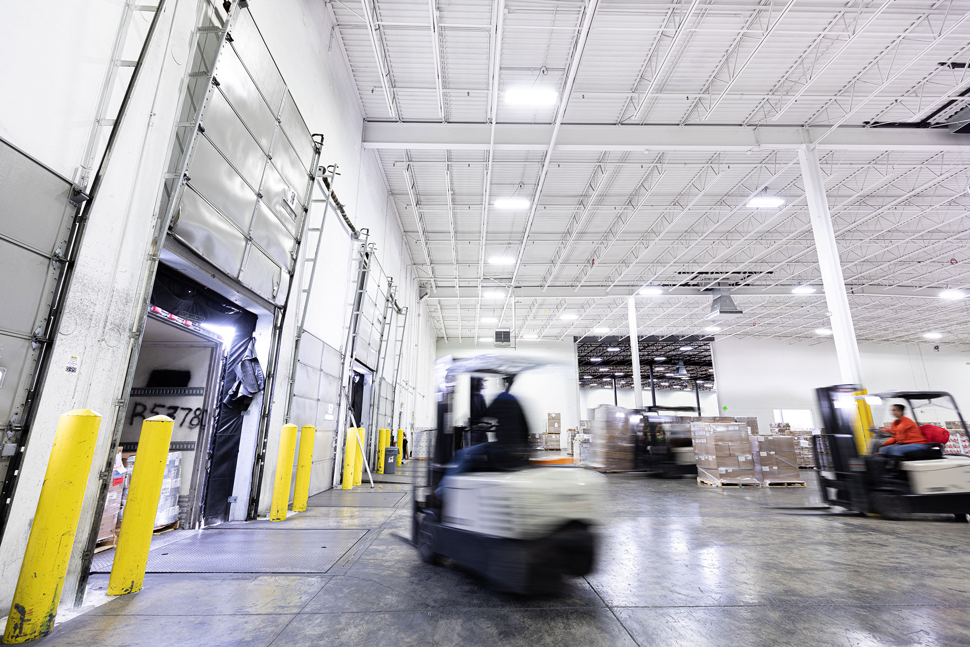 Two forklifts loading up a semi truck with freight at a warehouse loading dock.