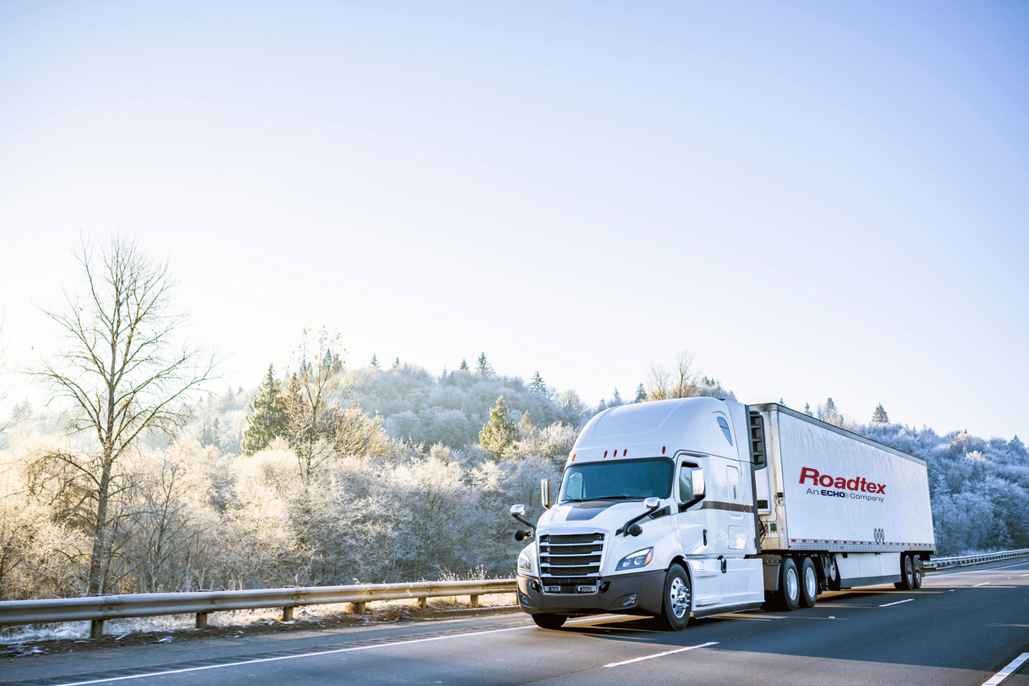 A white semi truck driving down a road during winter.